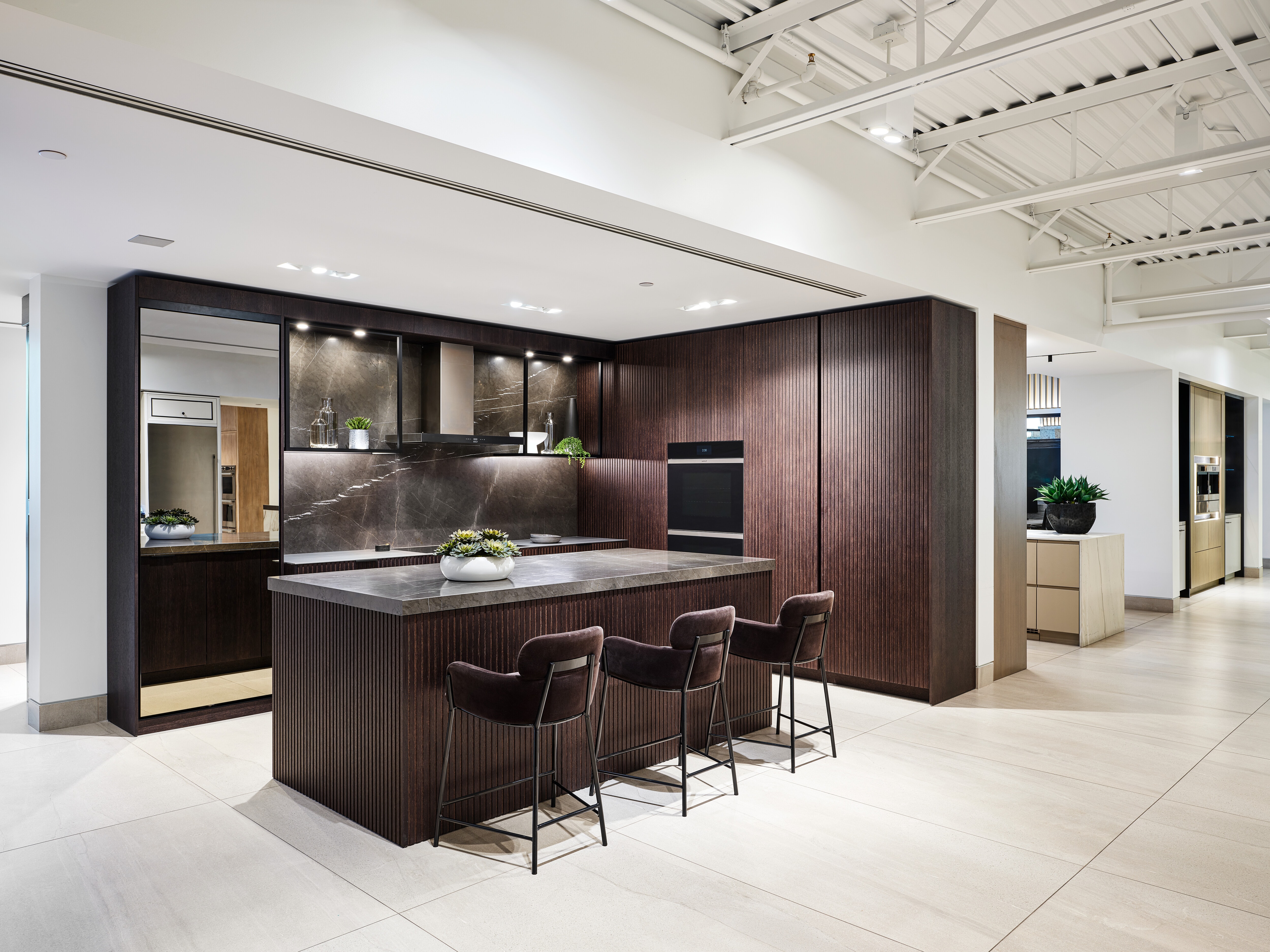 A brown and grey kitchen featuring brown chairs, a grey marble countertop and Wolf Appliance ovens.