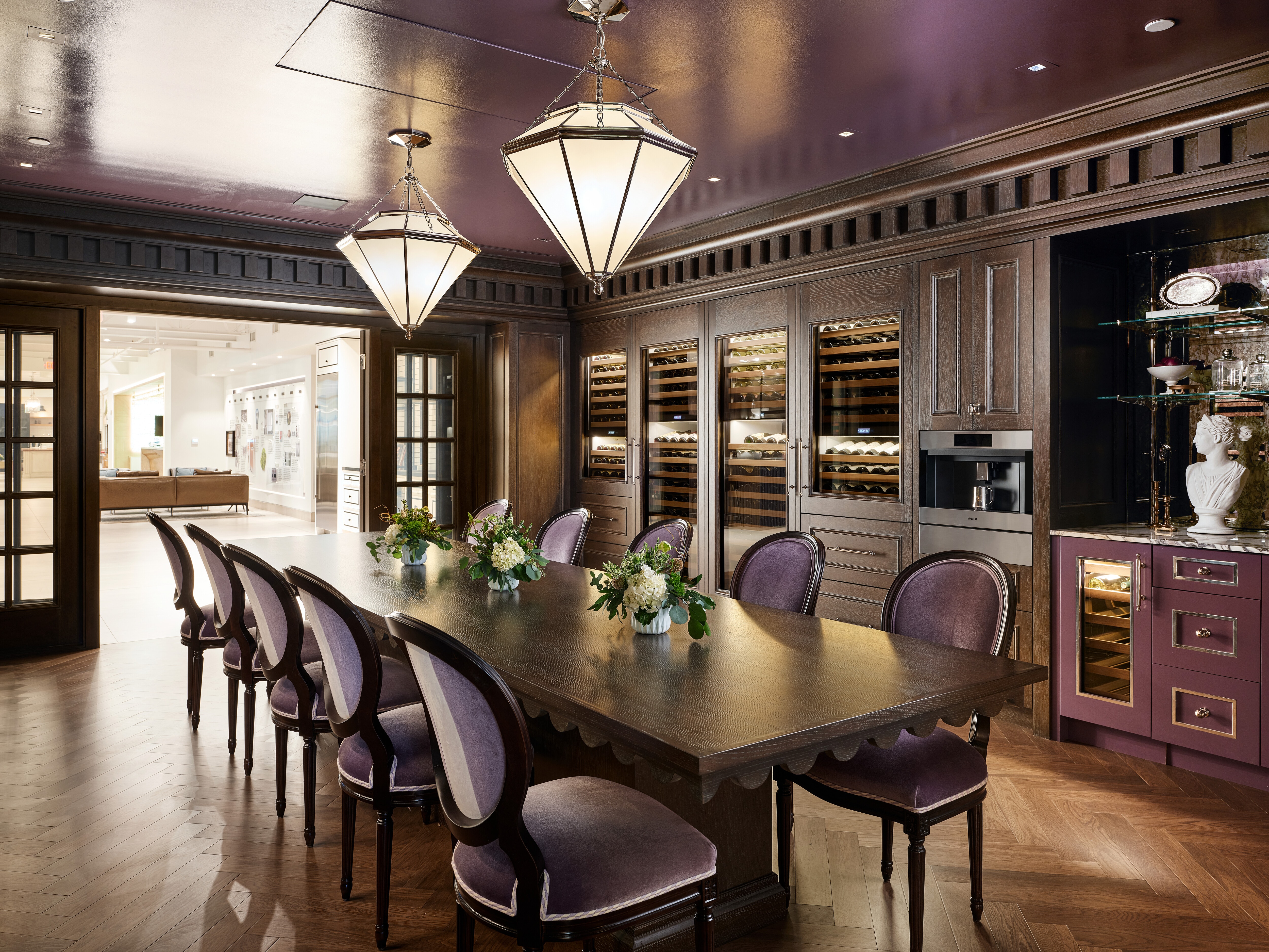 A fancy, luxury-styled kitchen with a brown wooden tabletop and light purple chairs with Sub-Zero wine refrigerators.