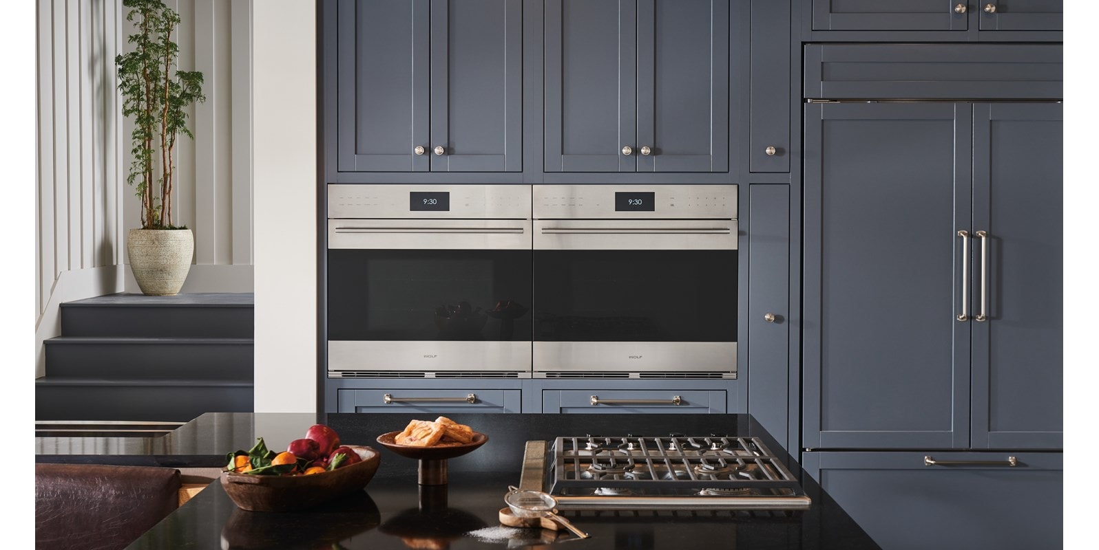 Wolf E Series (SO3050TE) Smart Wall Ovens installed side-by-side in an elegant cottage kitchen design featuring grey cabinetry with silver accent hardware.