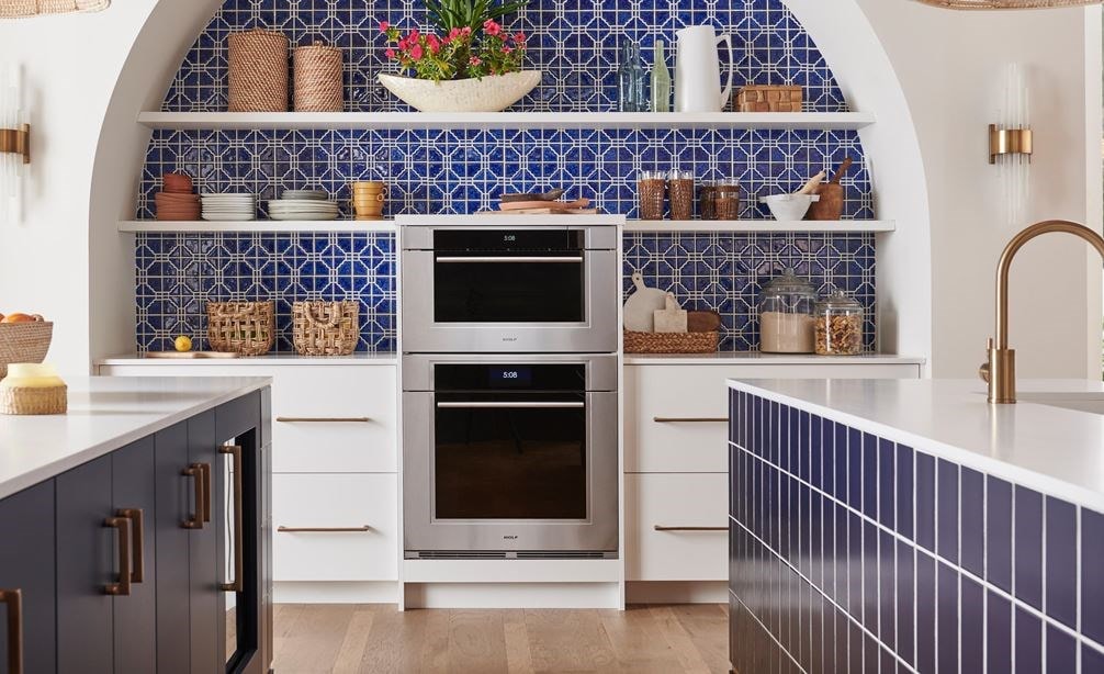 Wolf M Series Transitional Convection Steam Oven (CSO3050TM/S/T) shown in a bright and open Mediterranean kitchen design featuring blue mosaic tile backsplash, white open shelves, pendant lights and gold cabinet handles