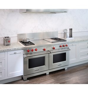 The Wolf 60" Dual Fuel Range 4 Burner Infrared Griddle French Top (DF604GF) shown with granite counter tops and country kitchen cabinets.