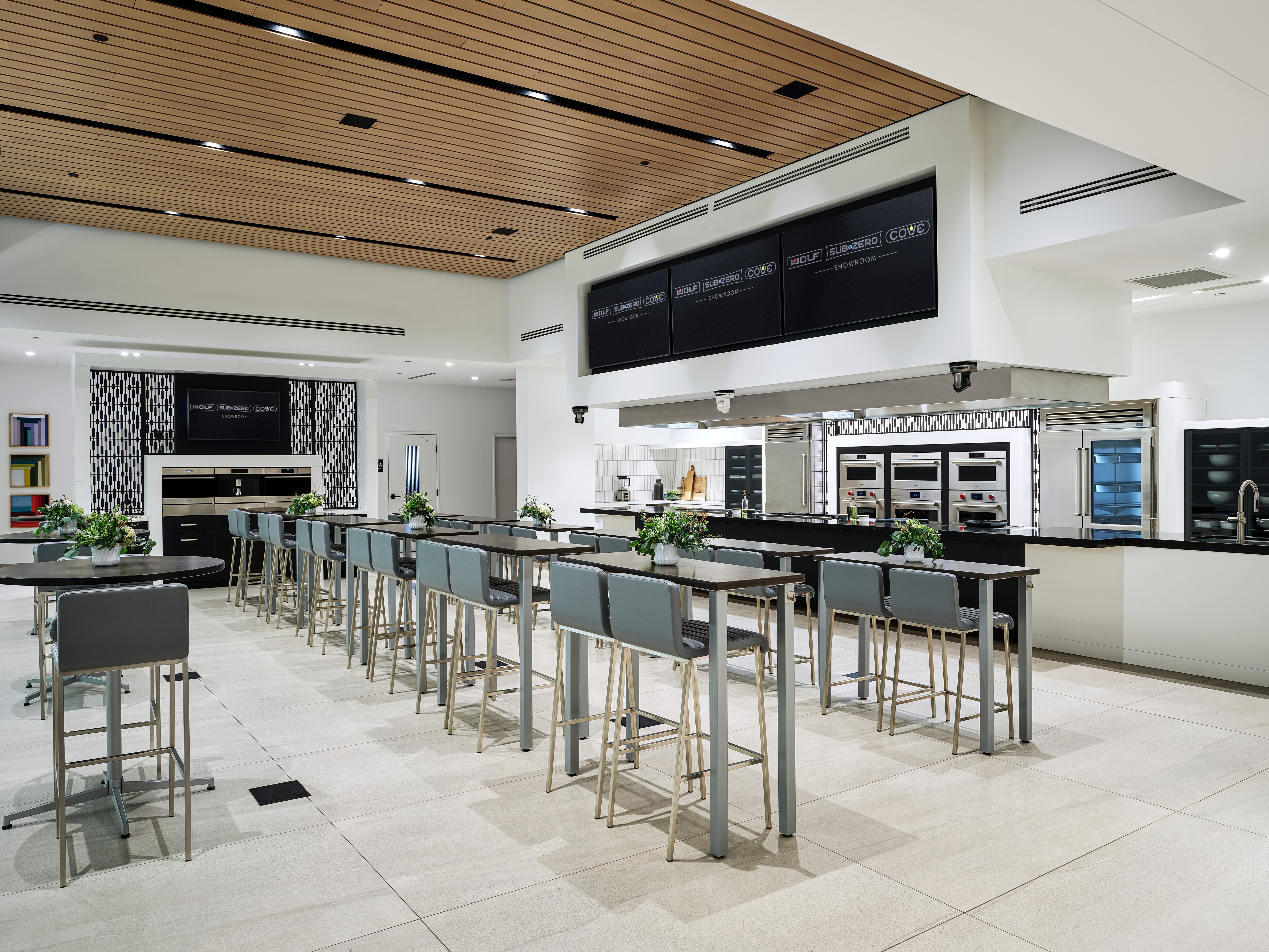 Built-In ovens by Wolf Appliances cover the walls next to a Sub-Zero refrigerator with blue-colored tall chairs.