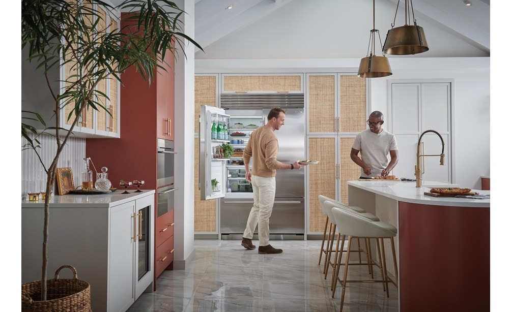 Two men smiling as they grab fresh food from their Sub-Zero 48 inch french door Classic Series stainless steel Refrigerator