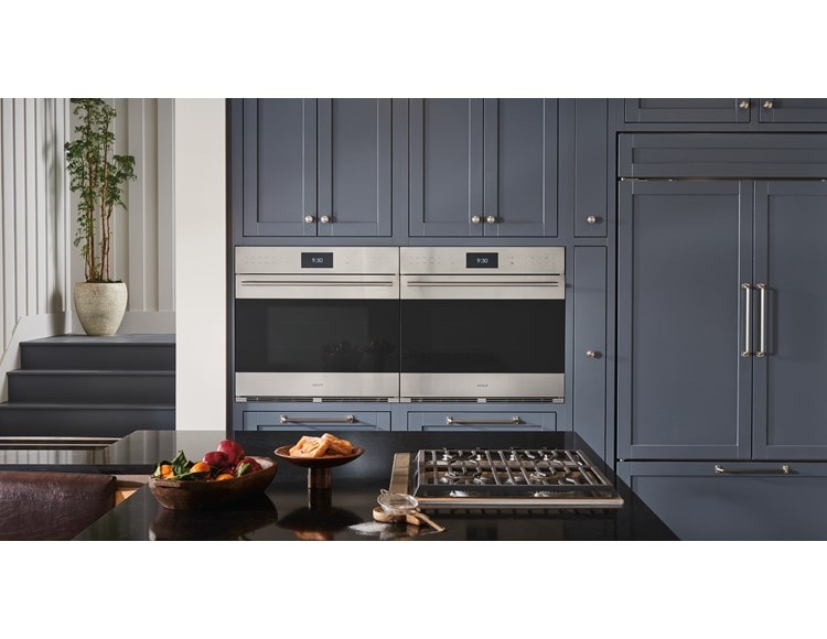Wolf E Series (SO3050TE) Smart Wall Ovens installed side-by-side in an elegant cottage kitchen design featuring grey cabinetry with silver accent hardware.