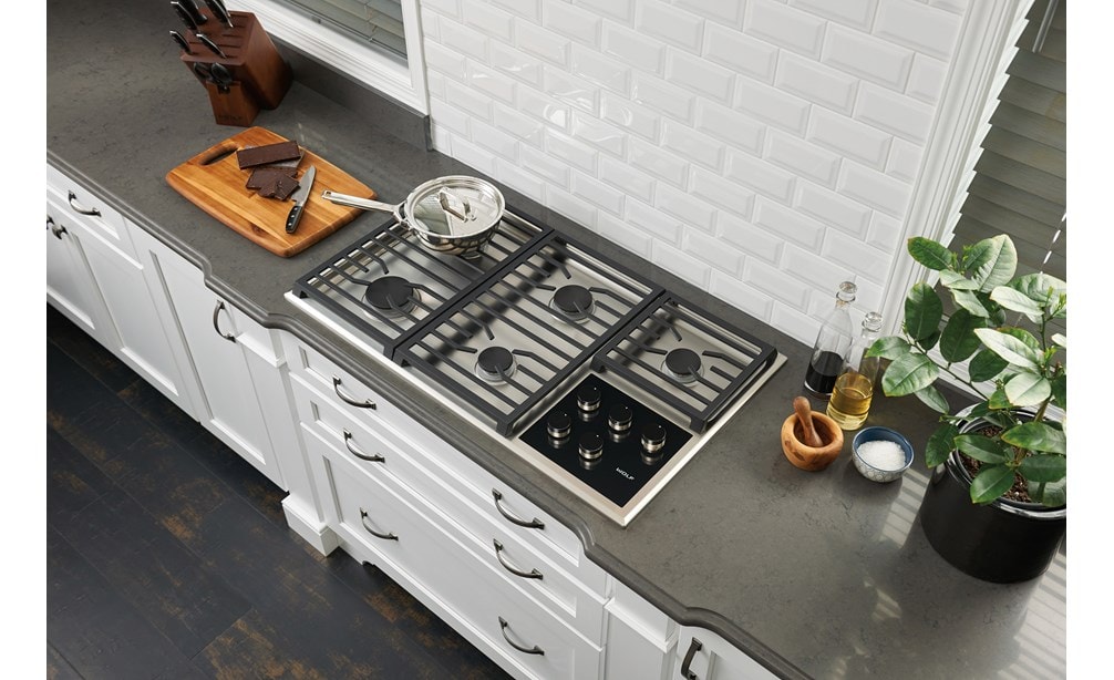 La surface de cuisson au gaz Wolf 36 po de style transitionnel à 5 brûleurs (CG365T/S) est centrée sur un comptoir en granit lisse et épuré pour un design de cuisine classique