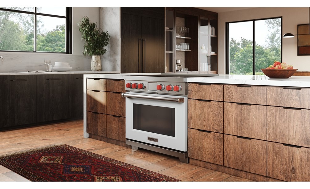 Wolf Professional Induction Range with white accent oven door and iconic red knobs set flush in white marble countertop in an open mid century modern kitchen design.