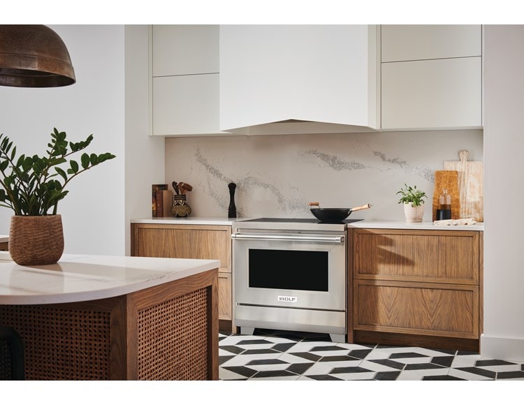 Cuisinière à induction Wolf 30/34 de style professionnel (IR30450/S/P) avec hotte murale Wolf blanche dans une cuisine moderne au sol carrelé noir et blanc.