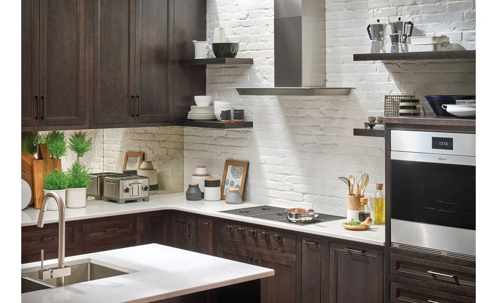 Hotte murale Wolf 36 po pour surface de cuisson - verre (VW36G) présentée contre des étagères en brique blanche apparente et des étagères flottantes dans un design de cuisine de luxe