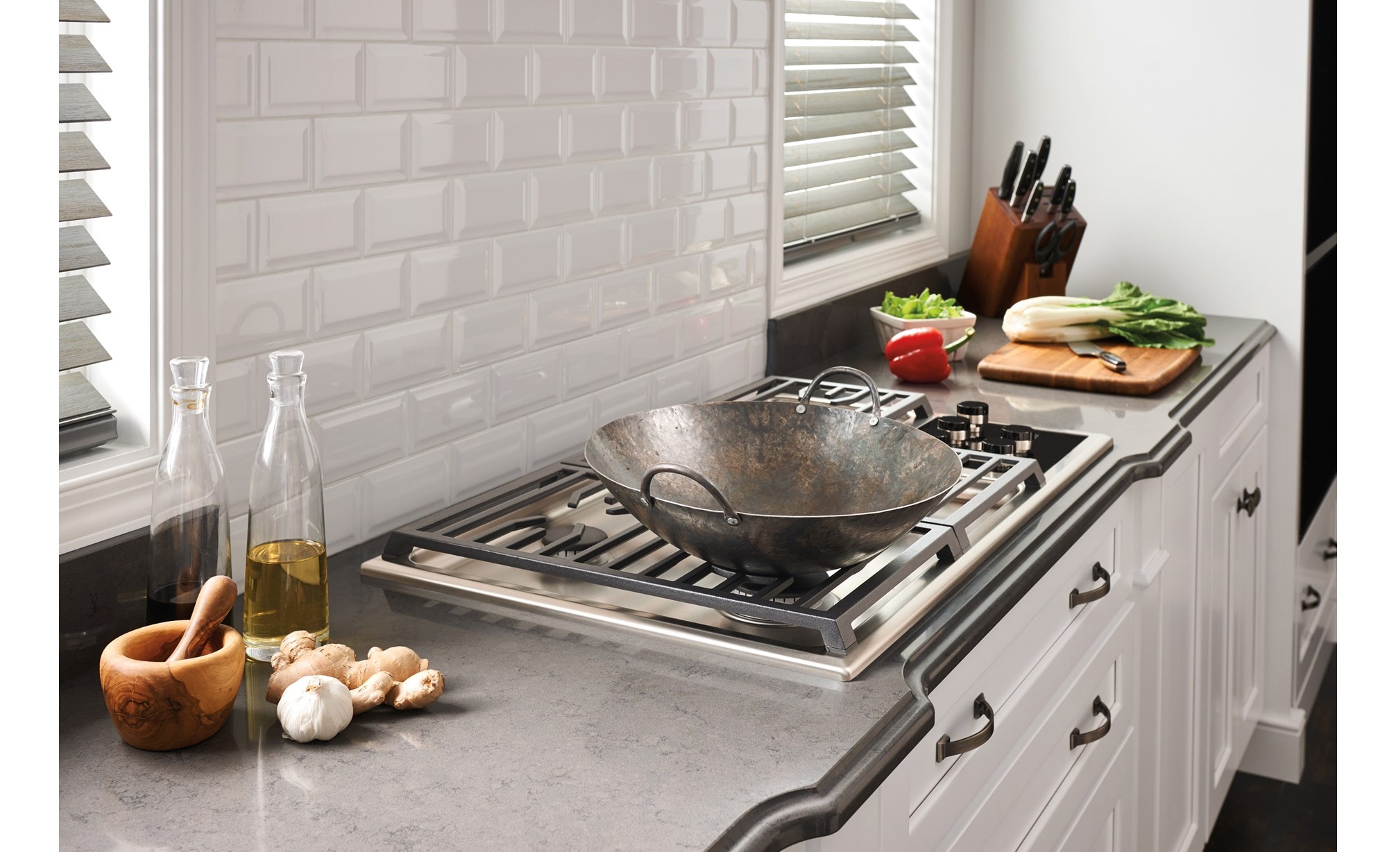 La surface de cuisson au gaz Wolf 36 po de style transitionnel à 5 brûleurs (CG365T/S) est centrée sur un comptoir en granit lisse avec un dosseret en briques blanches texturées
