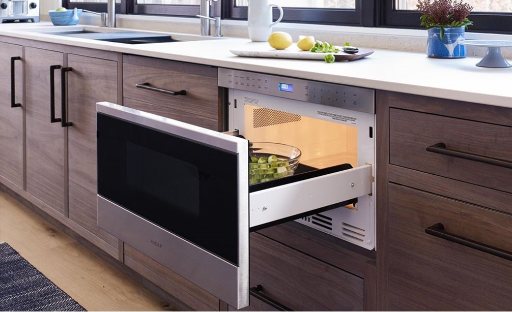 Le four à micro-ondes à tiroir de style transitionnel Wolf 24 po (MD24TE/S) ajoute une touche de confort dans les armoires en bois chaud sous les comptoirs blancs dans la cuisine moderne