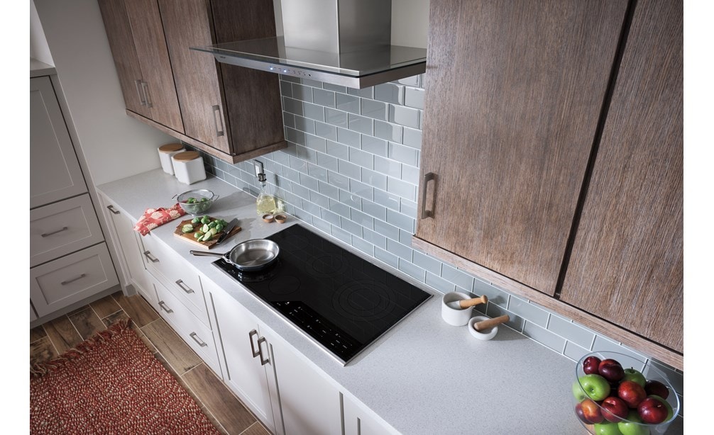 La hotte murale Wolf 36 po pour surface de cuisson - verre (VW36G) est présentée dans un design de cuisine confortable avec des armoires en bois aux tons chauds et un dosseret en carrelage