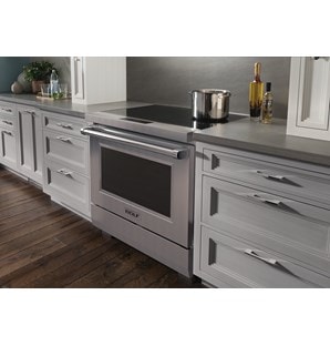 Cuisinière à induction Wolf 36/34 de style professionnel(IR36550/S/P) présentée dans des armoires grises avec un pot en acier inoxydable sur la surface de verre noir en céramique.